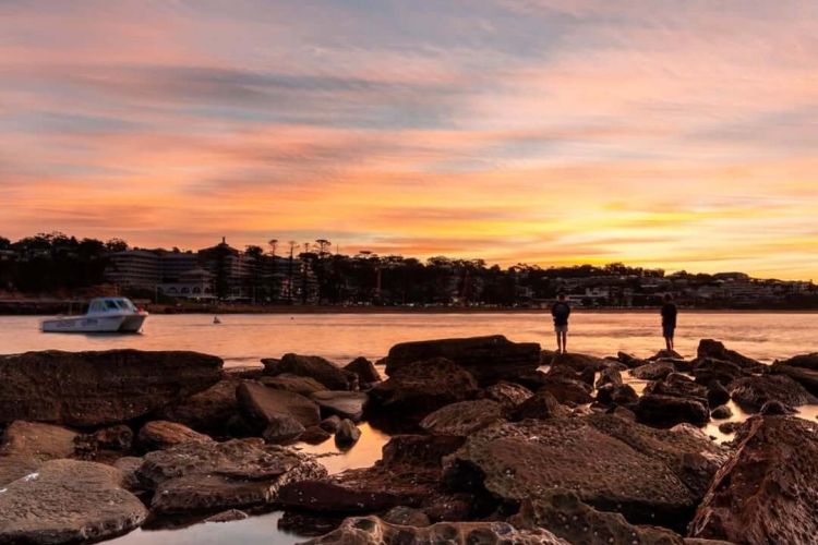 A rock platform with sunset casting itself over the ocean with a boat floating in the distance.